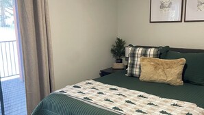 A bedroom with a bed, a bench, a nightstand, a potted plant, and two framed pictures on the wall.