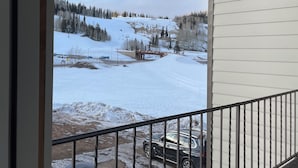 A balcony with a view of a snowy landscape, a parked car, and a building with white siding.