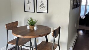A dining area with a round wooden table, two chairs, and a small plant on the table. There are four framed pictures on the wall above the table.