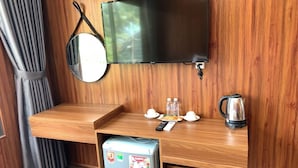 A compact room with a wooden desk, a flat-screen TV, a small fridge, a kettle, and a mirror. - PV BEACH BUNGALOW (Phu Quoc)