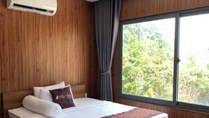 A modern bedroom with a wooden headboard, a large bed with white bedding and a brown throw, an air conditioning unit above the bed, and a large window with curtains. - PV BEACH BUNGALOW (Phu Quoc)