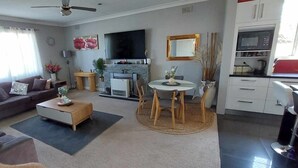 Un salon comprenant un canapé, une table basse et un coin repas avec des chaises et une table. On y trouve également une cheminée, un téléviseur et des meubles de cuisine.