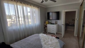 Une chambre à coucher comprenant un lit, une télévision, une commode et une porte donnant sur une autre pièce.