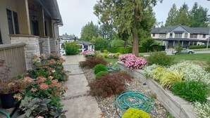 Zona residencial amb cases, un jardí ple de plantes i flors, i una entrada de cotxes.