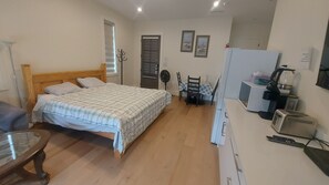 A bedroom with a wooden bed, a desk with a computer, a chair, and a refrigerator. - Self Contained Master Suite (Surrey)