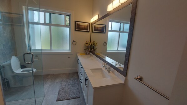A bathroom with a glass shower enclosure, a toilet, a sink with a mirror, and two potted plants.