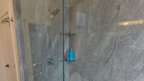 Un bany modern amb dutxa tancada amb vidre, parets de marbre i un vàter.