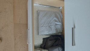 Vista des de dalt d'una habitació amb terra de fusta, un llit amb roba de llit blanca i gris, i un armari blanc.