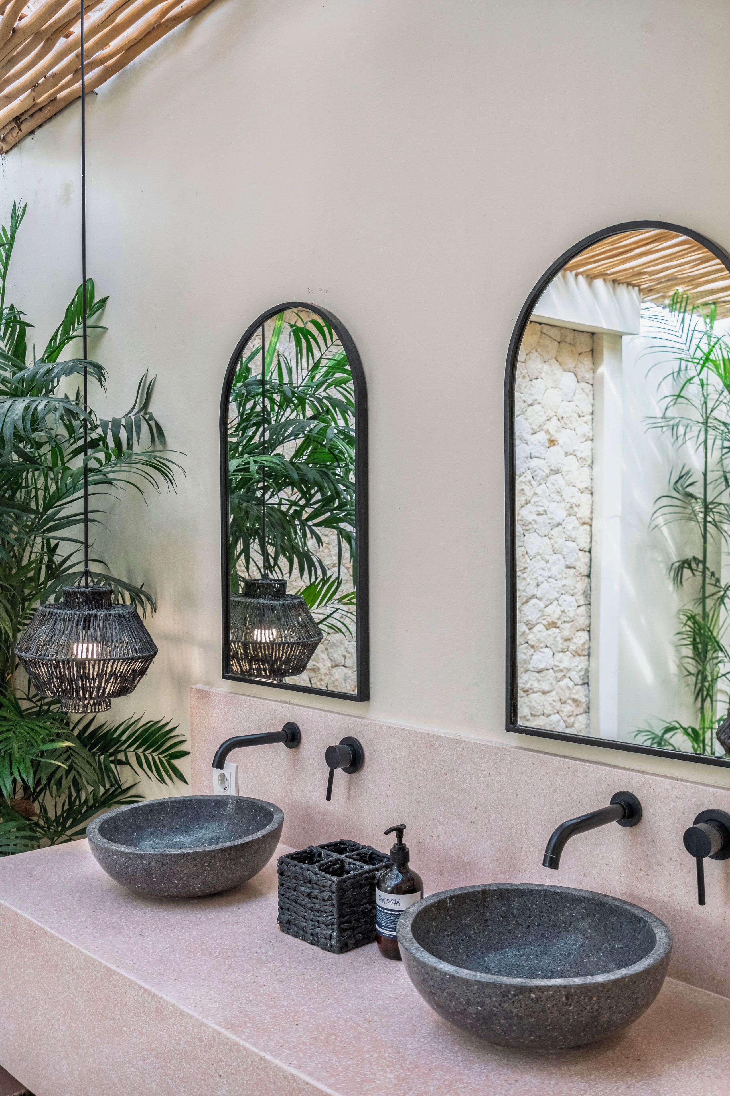 A bathroom with two stone sinks, a mirror, and hanging plants.