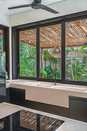 Un baño moderno con un ventanal grande, un ventilador de techo y un lavabo con cortina de ducha de bambú.