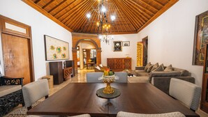 A spacious room with a large wooden dining table, comfortable seating, and a decorative centerpiece. - Puri Kantor Legacy (Ubud)