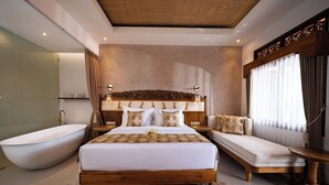 A modern bedroom with a large bed, a wooden headboard, a sitting area, a bathtub, and a large window with curtains. - Puri Kantor Legacy (Ubud)