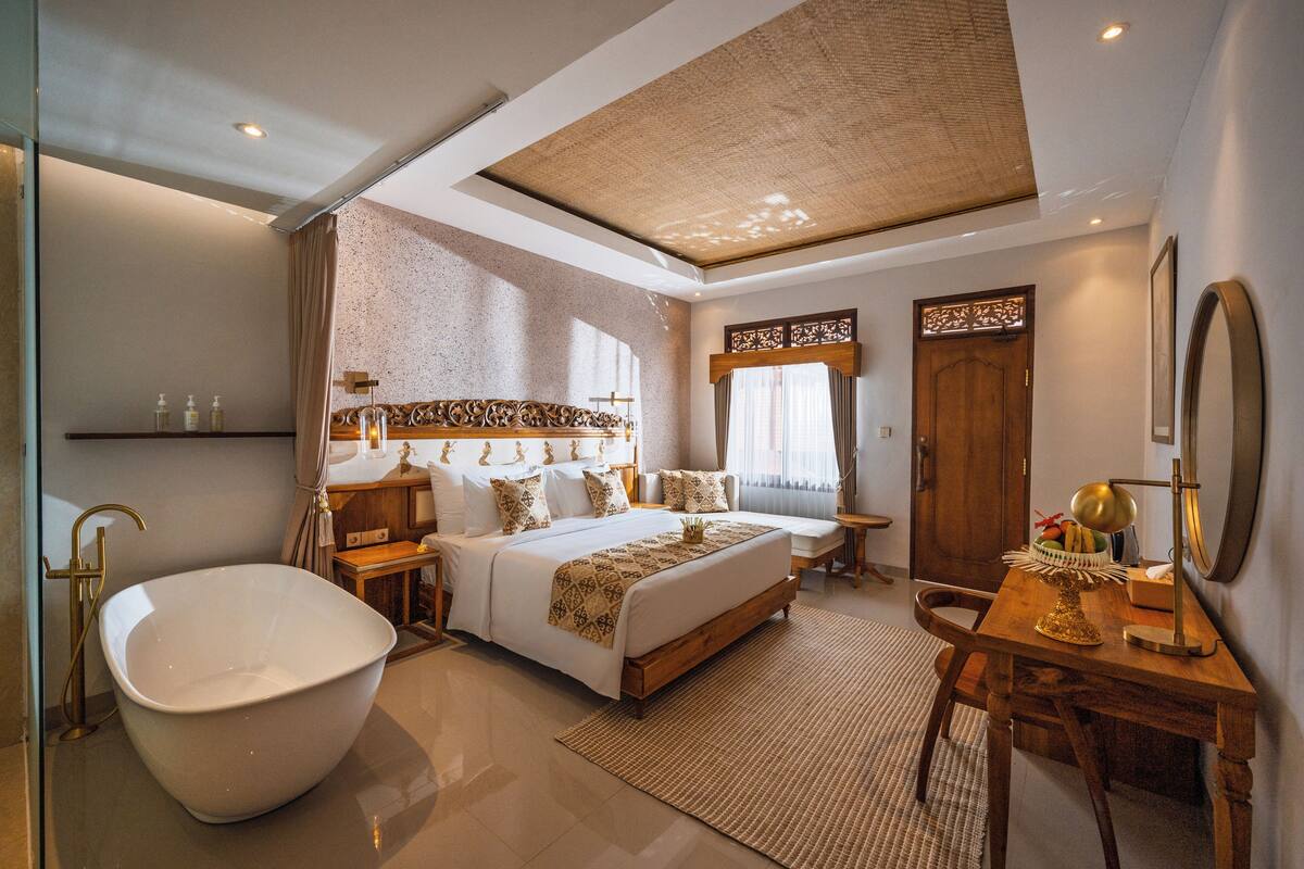 A modern hotel room with a large bathtub, a wooden desk, and a comfortable bed.