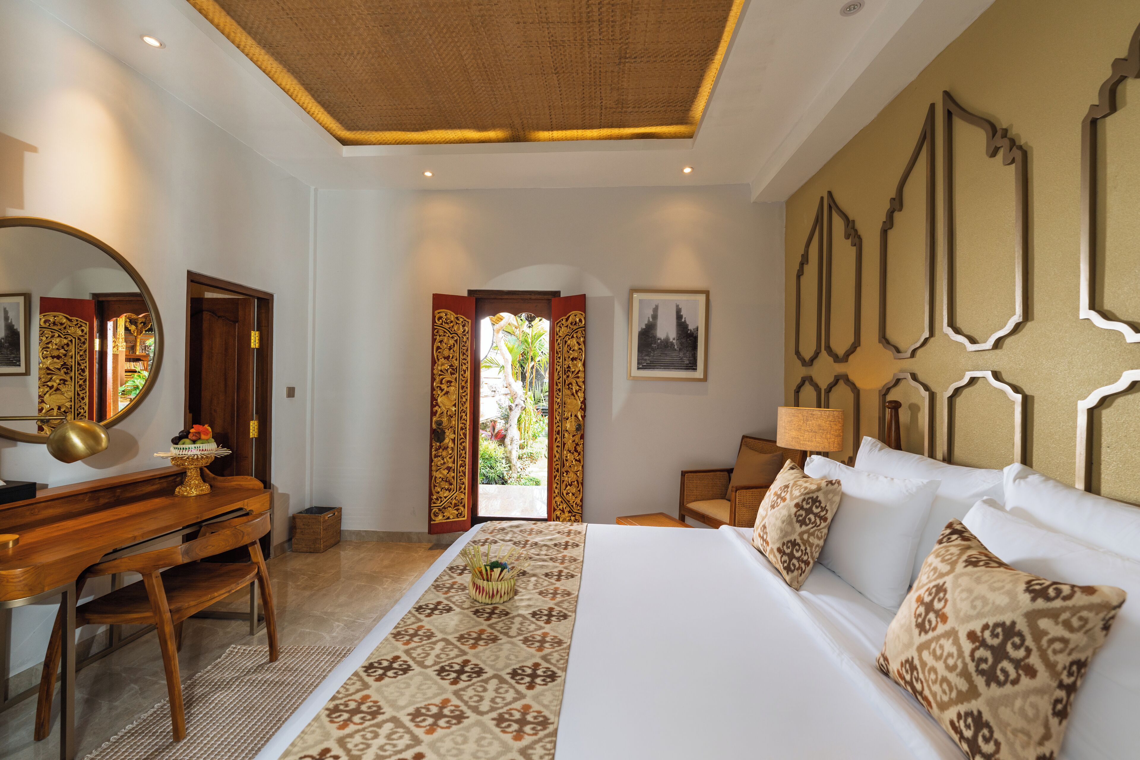 A hotel room with a bed, a desk, a chair, a mirror, and a door.