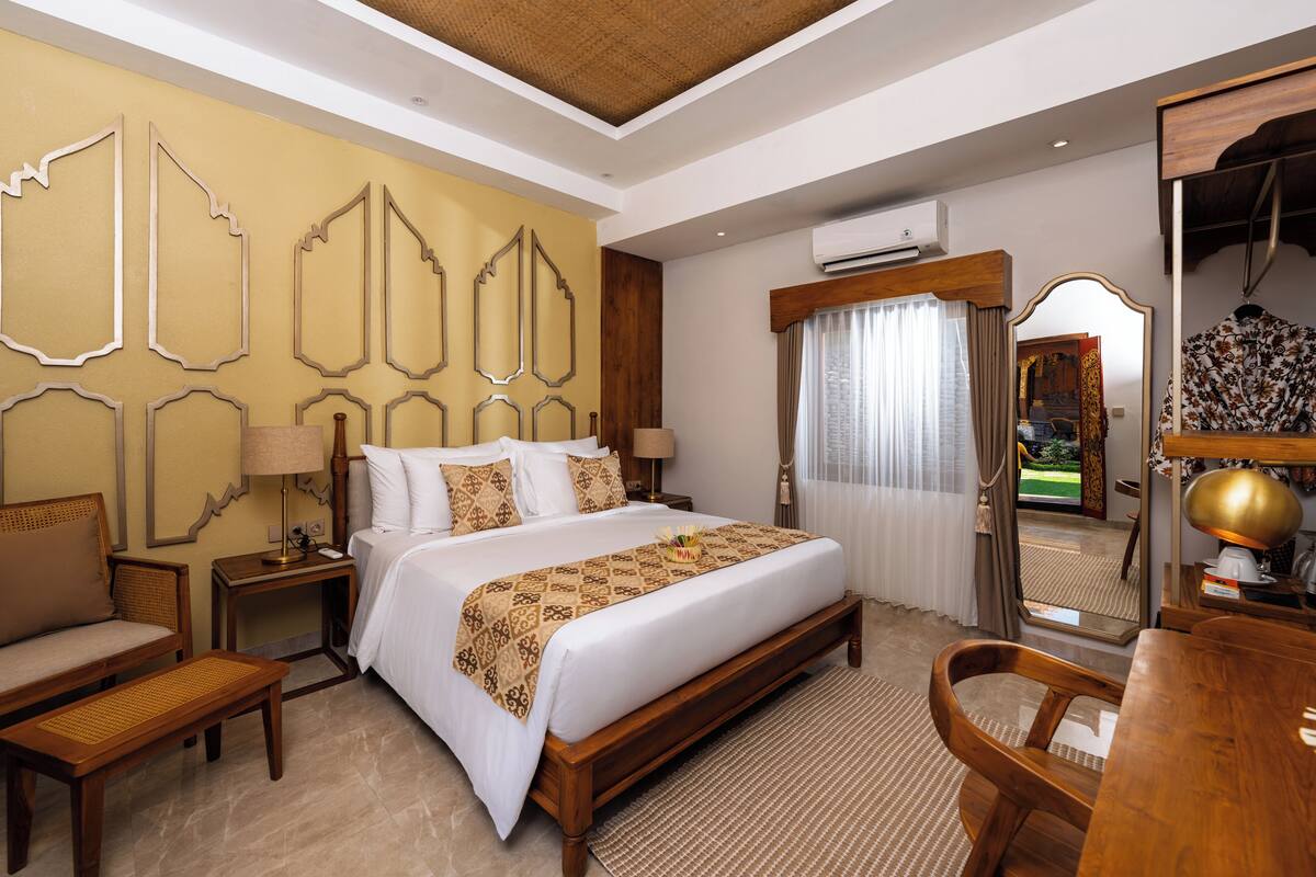 A hotel room with a large bed, wooden furniture, a mirror, and a view of the outdoors.