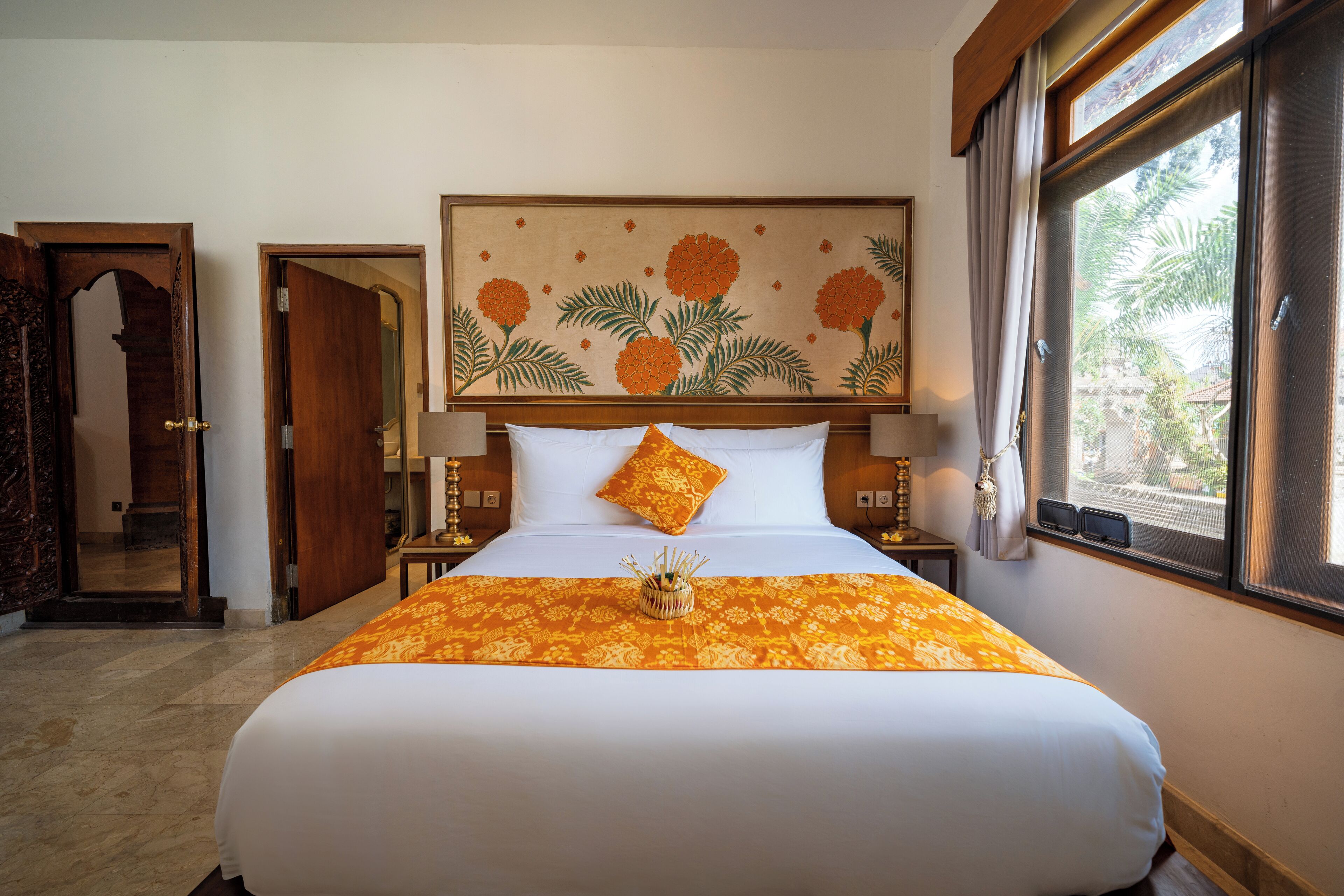 Una habitación de hotel con una cama grande, un cabecero decorativo, una ventana con vistas y una puerta que da a otra habitación.