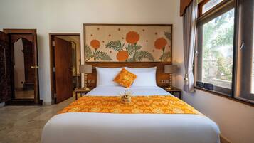 Una habitación de hotel con una cama grande, un cabecero decorativo, una ventana con vistas y una puerta que da a otra habitación.