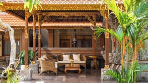 A traditional Balinese house with a covered porch, a sofa, and a small table. - Puri Kantor Legacy (Ubud)