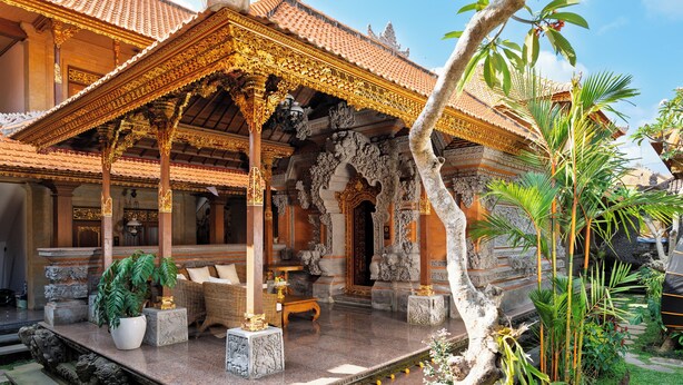 A traditional Balinese temple with ornate architecture, a covered porch, and a garden area with plants and a small pond. - Puri Kantor Legacy (Ubud)
