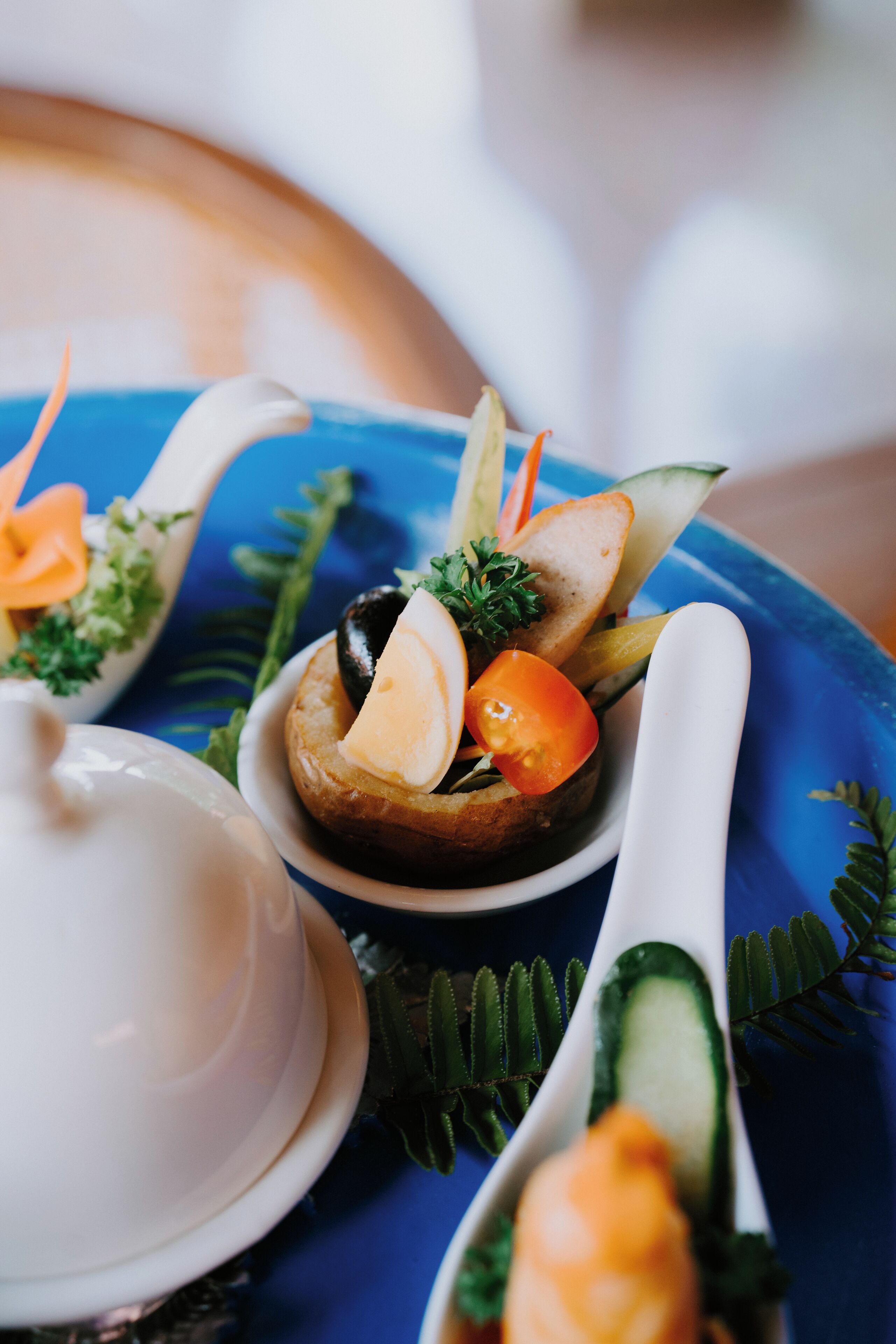 A close-up of a food arrangement with a white teapot and two white spoons on a blue tray.