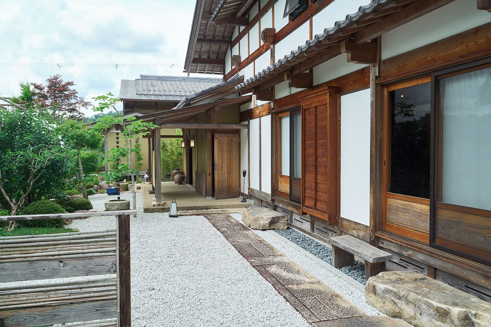 A traditional Japanese building with a wooden exterior, large sliding doors, and a gravel pathway leading to a wooden bench.