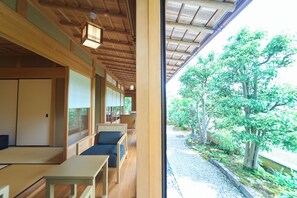 Ein traditioneller japanischer Raum mit Tatami-Boden, einem niedrigen Tisch und Blick auf einen Garten durch ein großes Fenster.