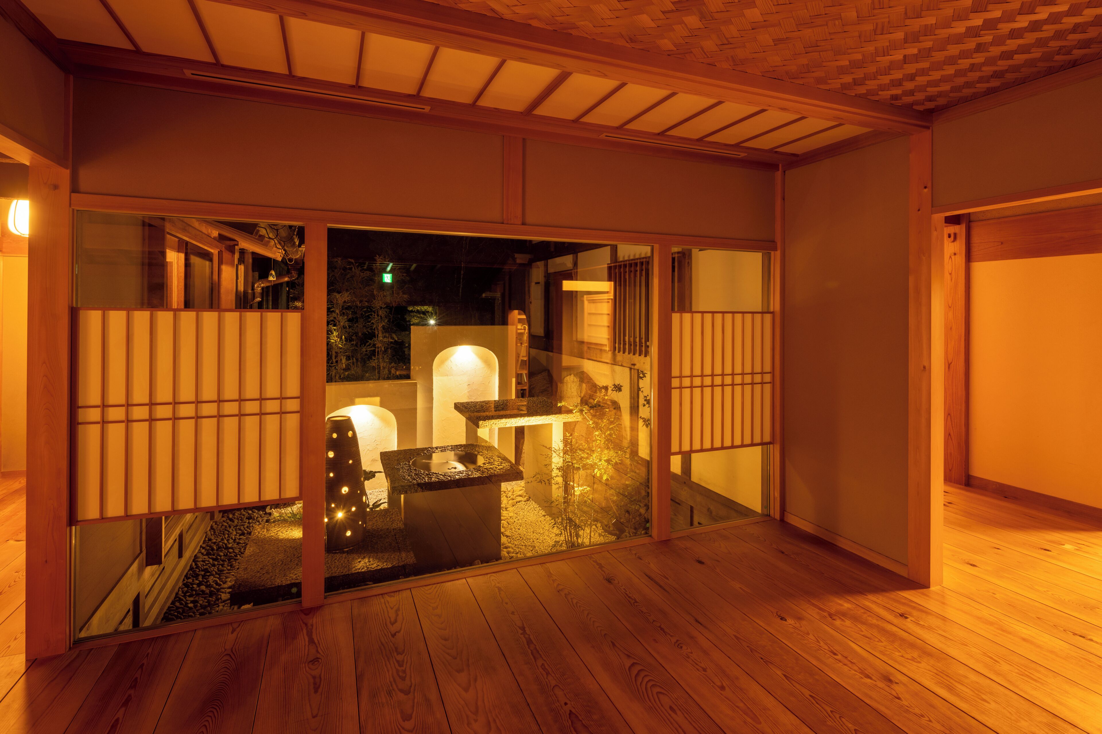 Une pièce de style japonais traditionnel, dotée de portes coulissantes, d’un sol recouvert de tatamis et d’un petit espace extérieur agrémenté d’une lanterne en pierre.