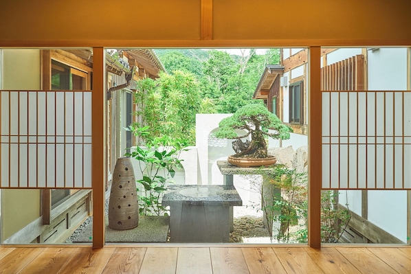 A traditional Japanese room with tatami flooring, a shoji screen, and a view of a garden with a bonsai tree.