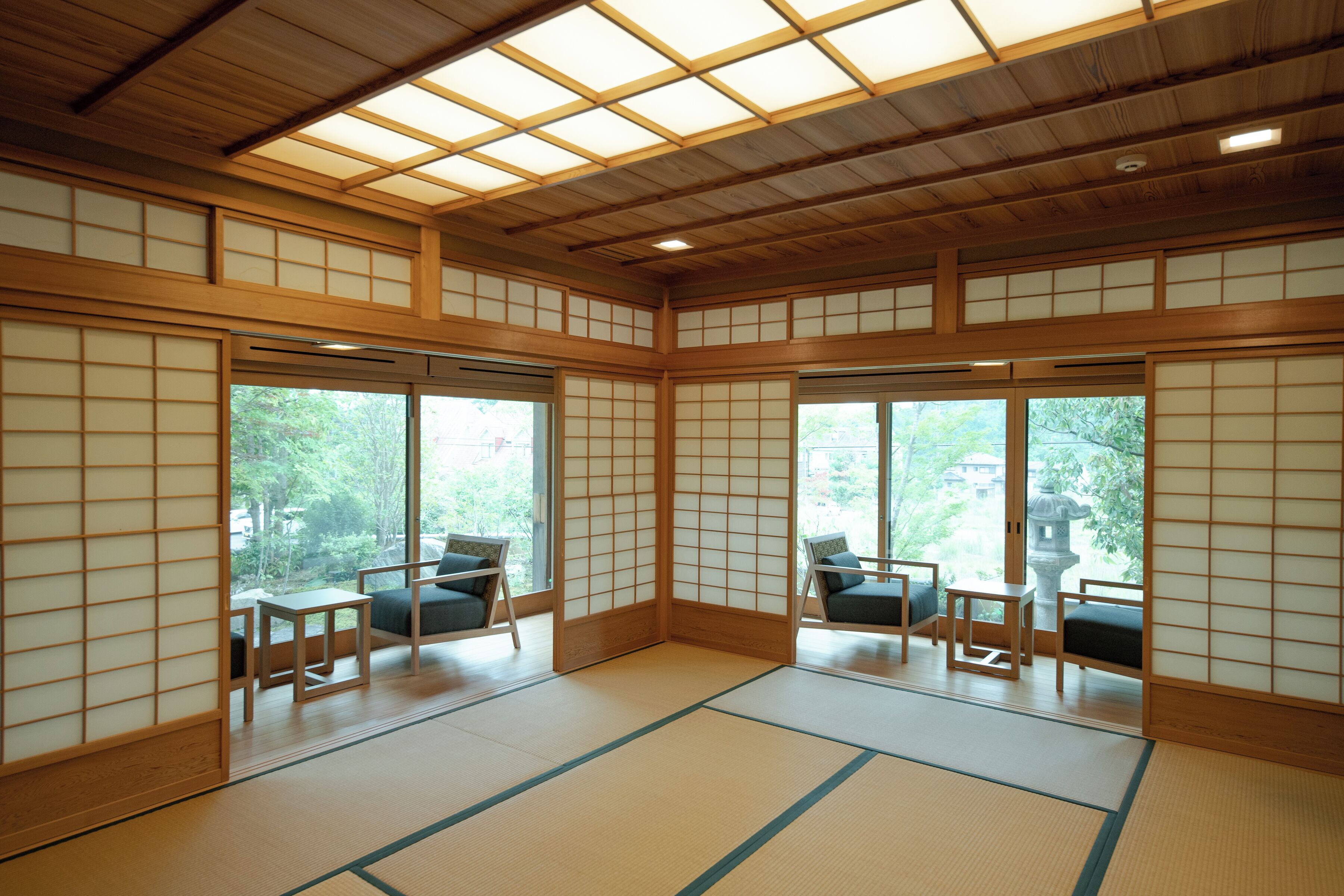 A traditional Japanese room with tatami flooring, sliding doors, and a view of greenery outside.