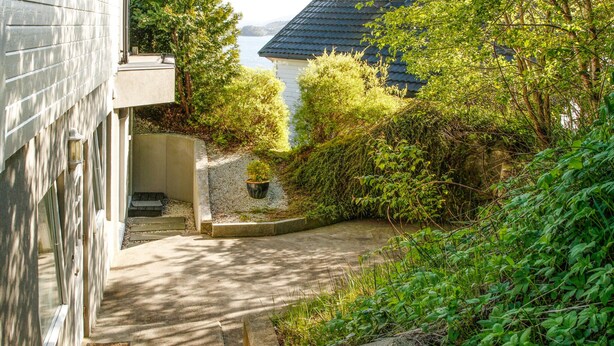 A narrow pathway leading to a house with a sloped roof, surrounded by dense greenery and a small garden area. - Gorgeous apartment with WiFi (Godvik)