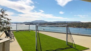 A patio with a netted play area, a seating area, and a view of a body of water and distant hills. - Gorgeous apartment with WiFi (Godvik)