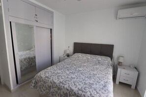 A bedroom with a bed, a wardrobe, a nightstand, and an air conditioner.