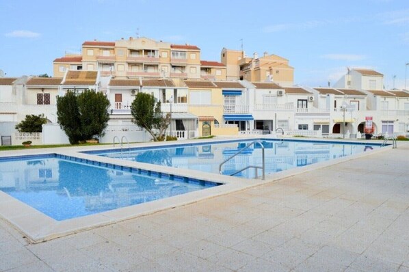 A swimming pool with a tiled deck, surrounded by multi-story buildings with balconies.