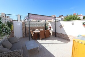 An outdoor patio area with a table and chairs, a sofa, and a covered seating area.