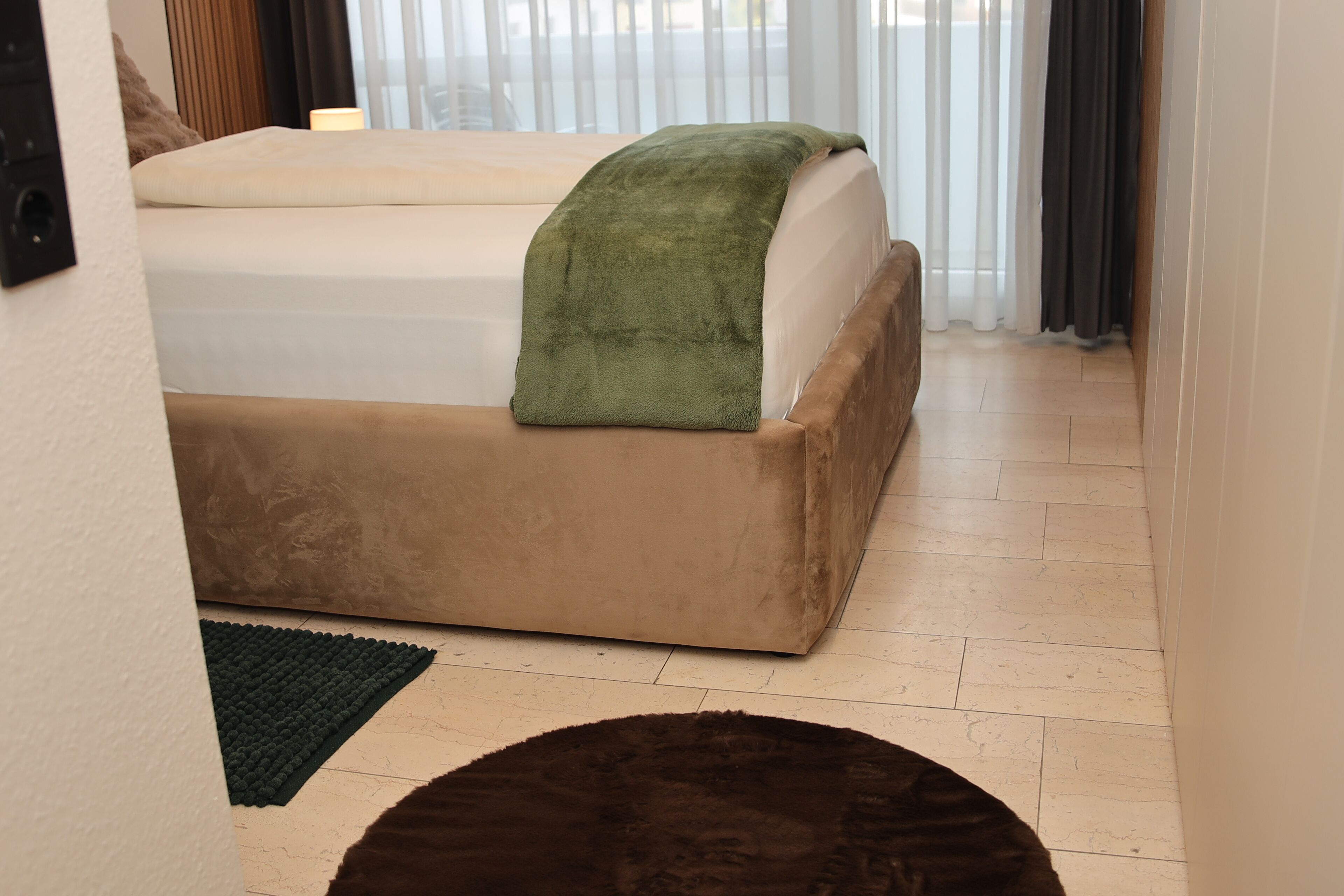 Ein Schlafzimmer mit einem Bett, einer grünen Tagesdecke, einem braunen Hocker und grünen sowie braunen Teppichen.