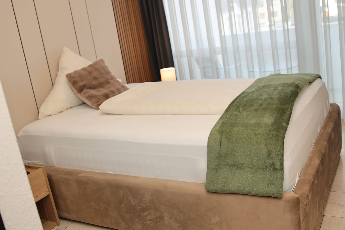 A bed with a green blanket, a brown pillow, and a white pillow.