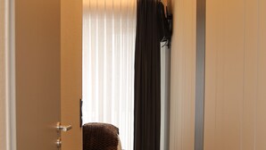 A narrow hallway with a wooden floor, a bed with a brown blanket, and a window with sheer curtains. - Hotel Hafez (Bad Salzuflen)