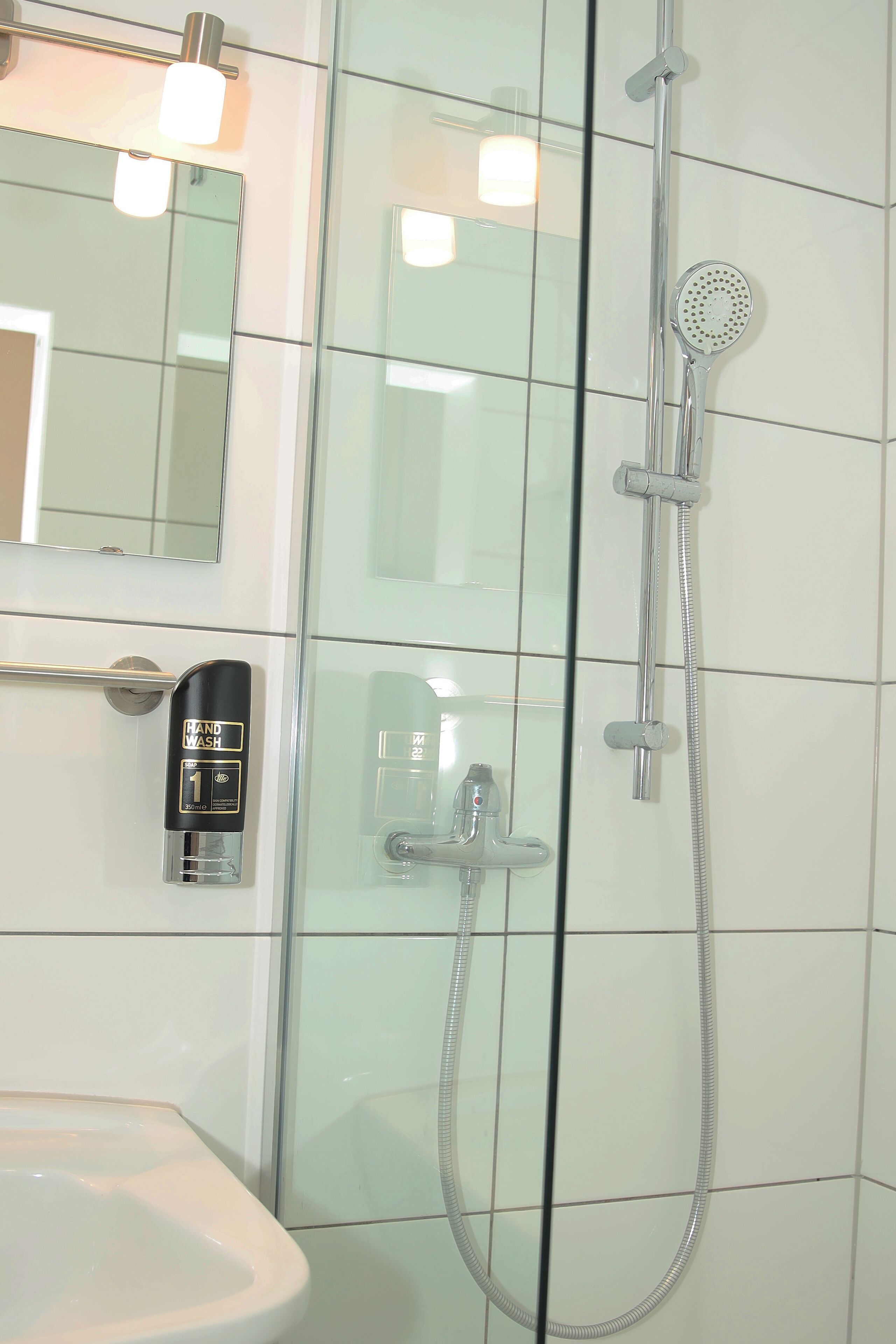 A glass-enclosed shower with a handheld showerhead and a handheld faucet.