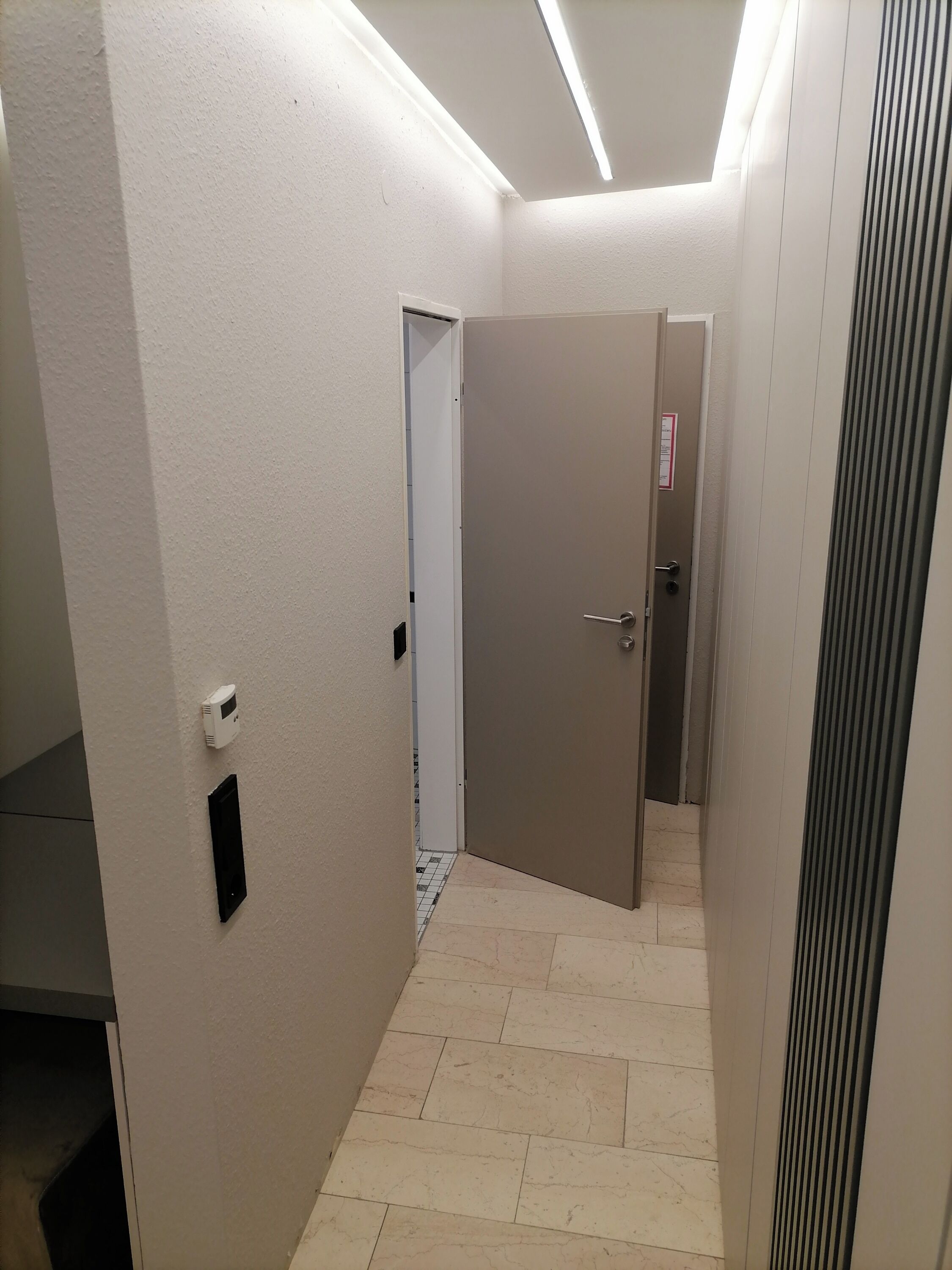A narrow hallway with a closed door, a thermostat on the wall, and a vent on the right.