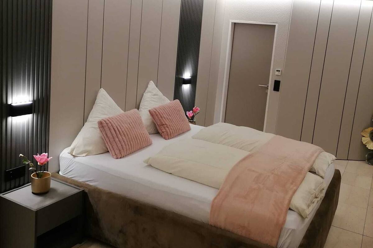A modern bedroom with a large bed, a bedside table, a nightstand, and a wall-mounted light fixture.