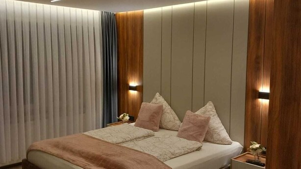 A modern bedroom with a large bed, wooden paneling, and built-in lighting. - Hotel Hafez (Bad Salzuflen)