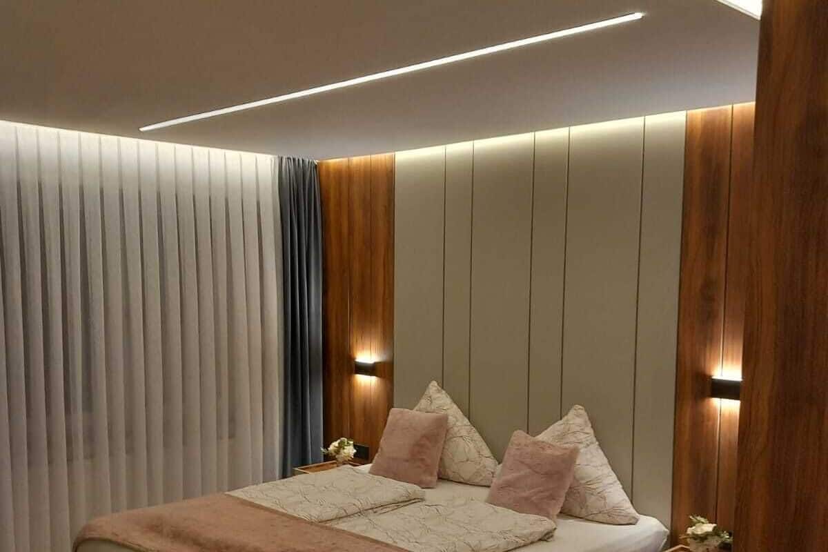 A modern bedroom with a large bed, wooden paneling, and built-in lighting.