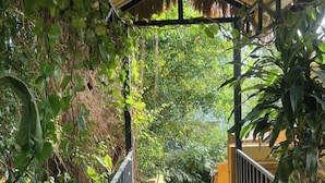 A wooden walkway with metal railings, surrounded by lush greenery and a thatched roof structure. - Eco Lagoon (Mang Yang)