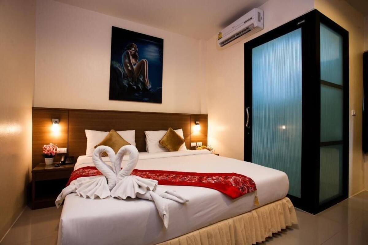 Una habitación de hotel con una cama grande, un cuadro en la pared, una mesita de noche con lámpara y una puerta corredera.