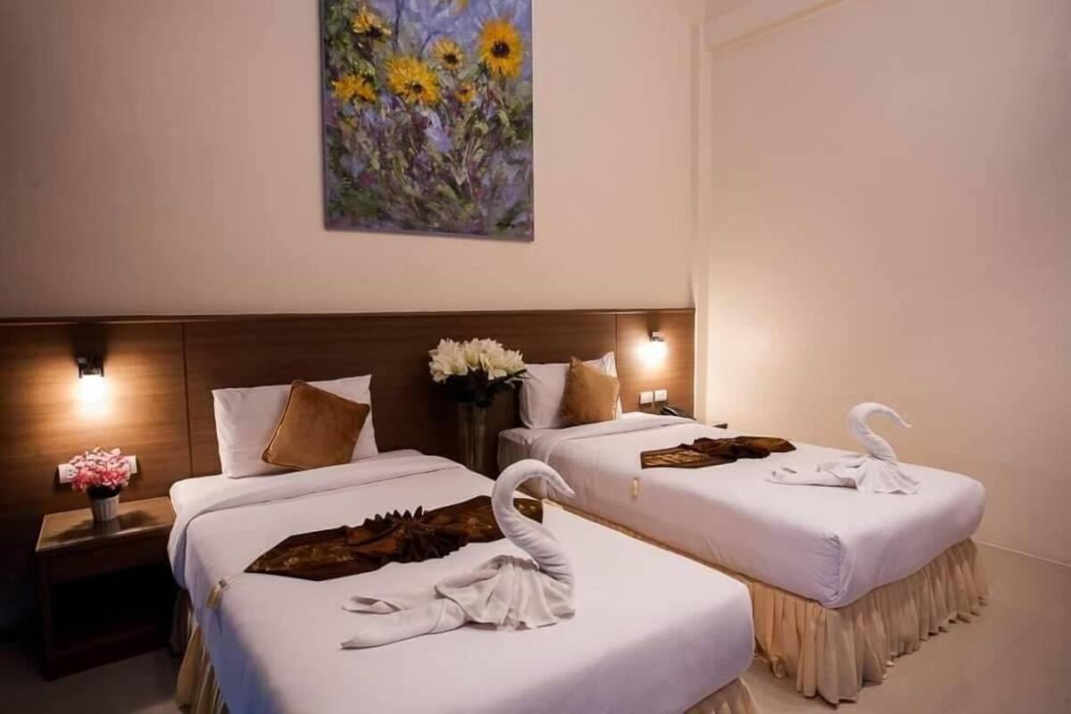Dos camas dobles con sábanas blancas, un cabecero de madera, un cuadro colgado en la pared con girasoles, una mesita de noche con un florero y una toalla con forma de cisne sobre las camas.