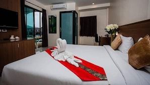 A hotel room with a neatly made bed, a flat-screen TV, a wooden cabinet, and a large window offering a view. - Royal Waves Hotel (Patong)