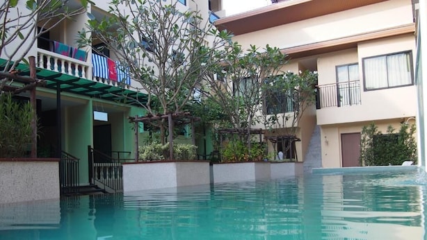 A swimming pool with a clear blue water surface, surrounded by a building with balconies and a covered area. - Royal Waves Hotel (Patong)