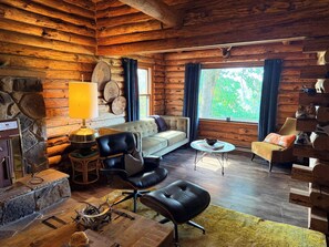 A log cabin interior with a sofa, chairs, a table, and a stone wall.