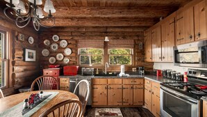 Una cocina rústica con armarios de madera, estufa, microondas y un comedor con mesa y sillas de madera.