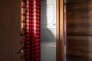 Una sala de bugaderia amb una rentadora blanca i una cortina amb quadres vermells i negres.